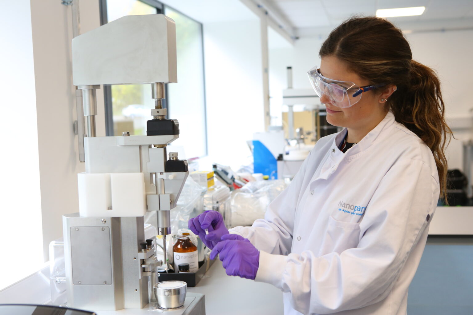Female scientist with long brown hair in a white lab coat holds powder filled capsule for inhalation product development.
