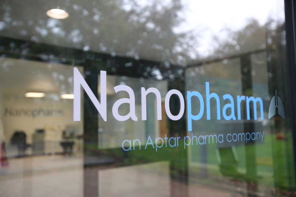 Glass front door to entrance of Nanopharm facility in the UK, with Nanopharm blue and grey wordmark and reflections.