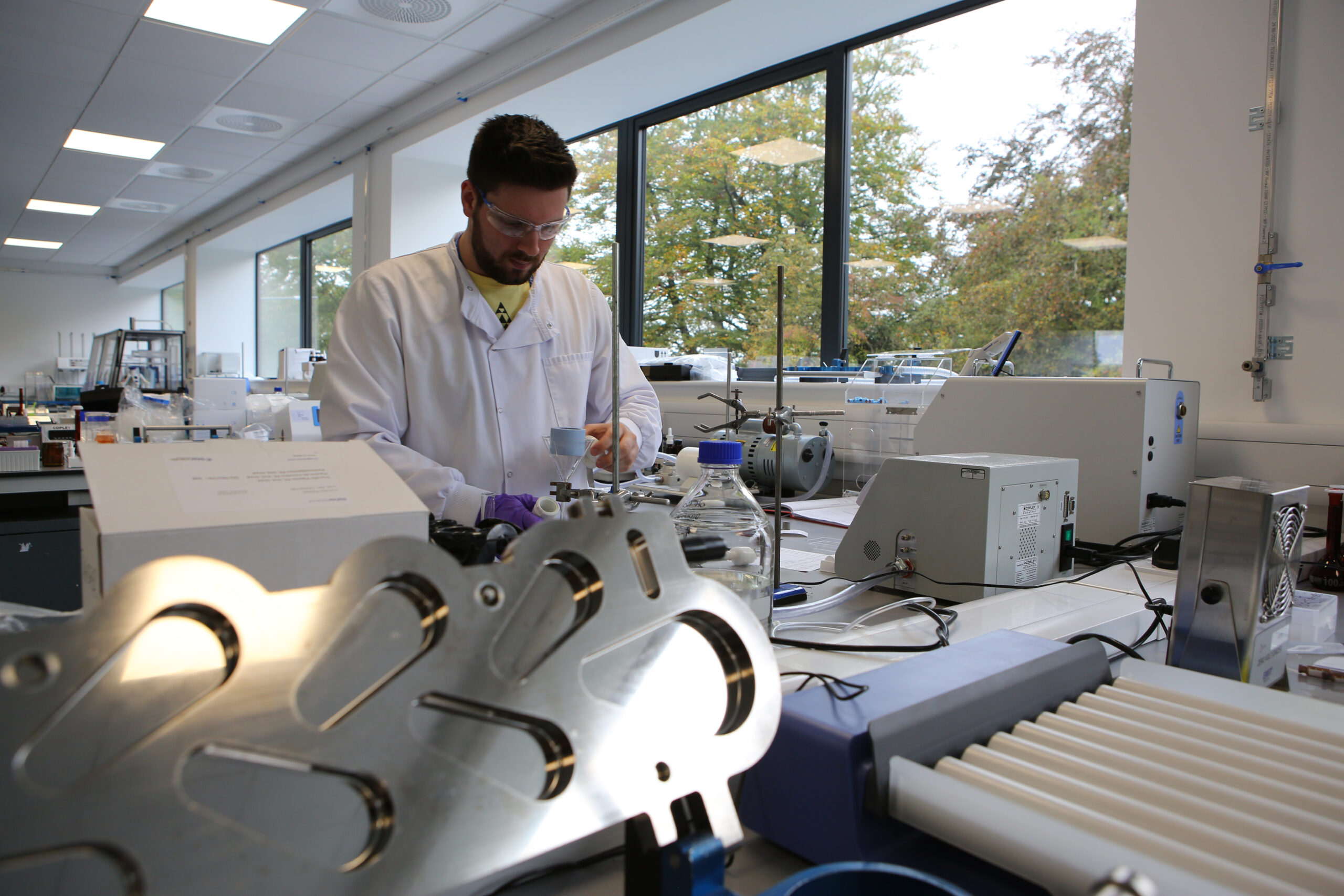 Nanopharm analyst stands behind stainless steel laboratory equipment in a white lab coat developing OINDPs.