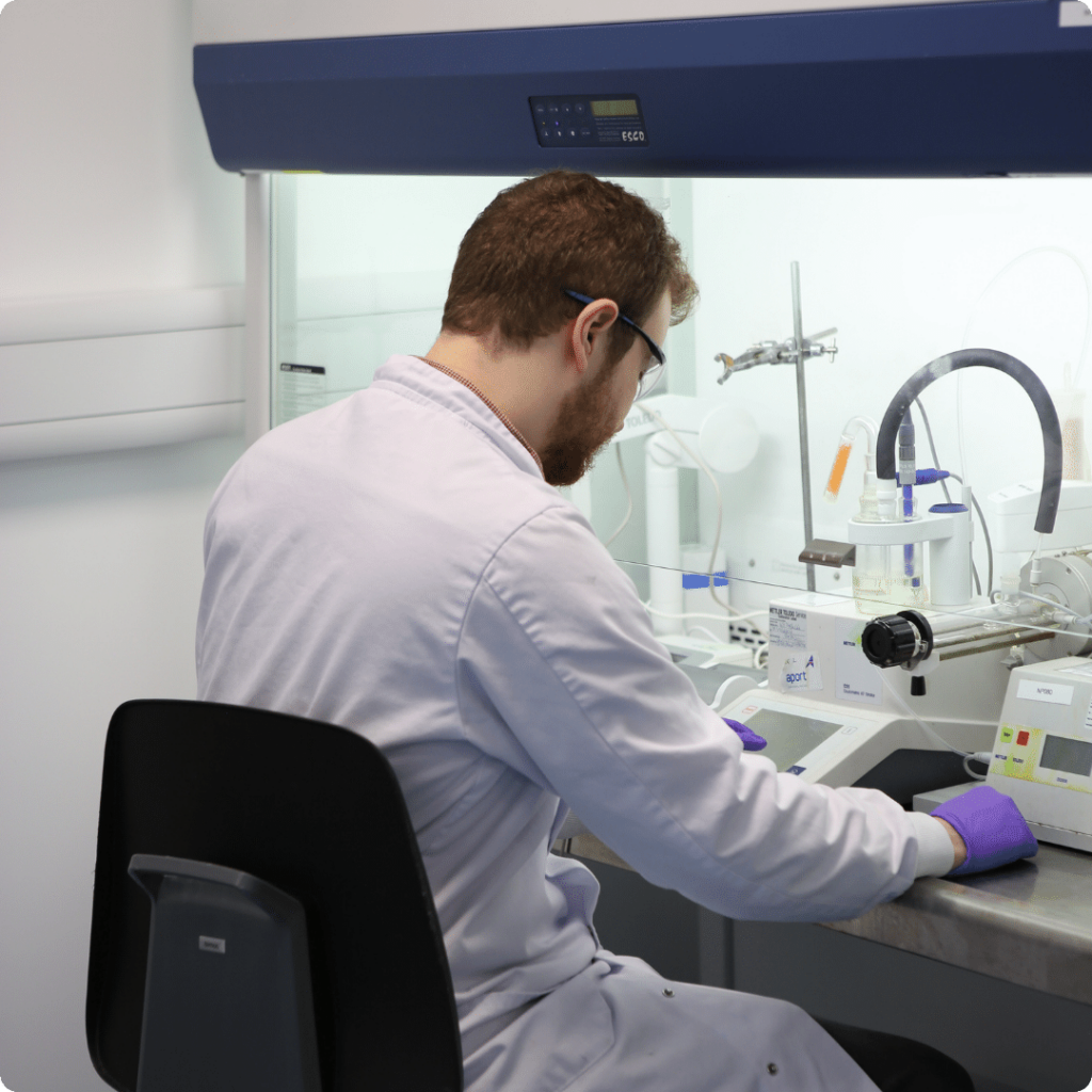 Seated Nanopharm scientist seated in from of a fume hood in lab coat and glasses performs inhaled biologic development.