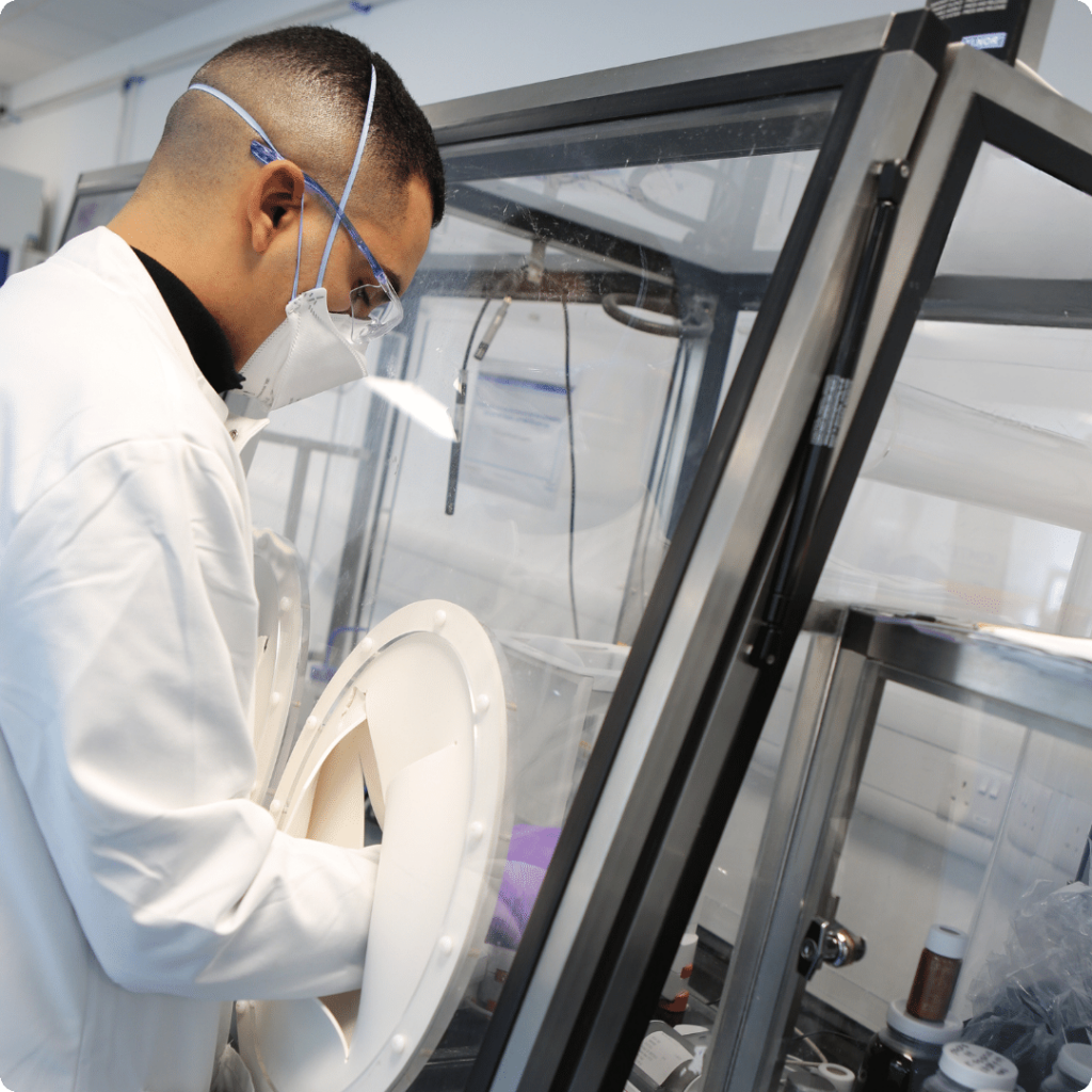 Male scientist in white lab coat and short brown hair uses a glove port in an isolator for OINDP development at Nanopharm.