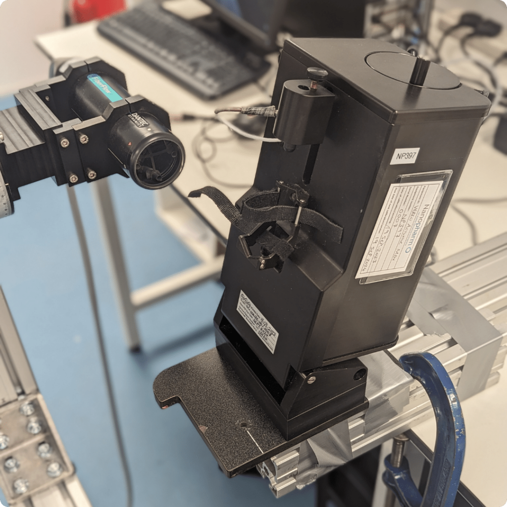 Black rectangular box on a stand that performs automated actuation for pMDI and other inhaler development at Nanopharm.